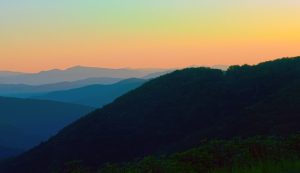sunset over the appalachian mountains the mountains are blue and the sky is a soft orange.